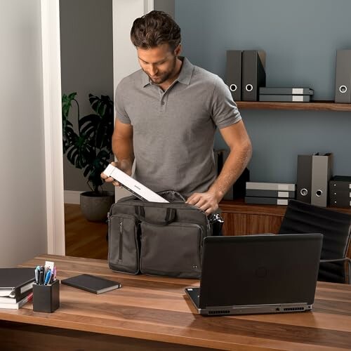 Man organizing office bag at desk with laptop.