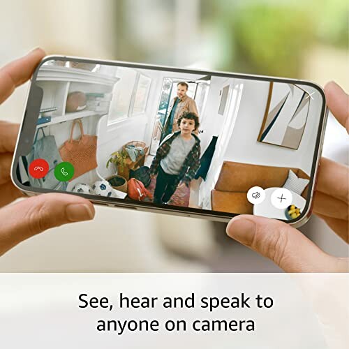 Person holding smartphone displaying video call with two people at a home entrance.